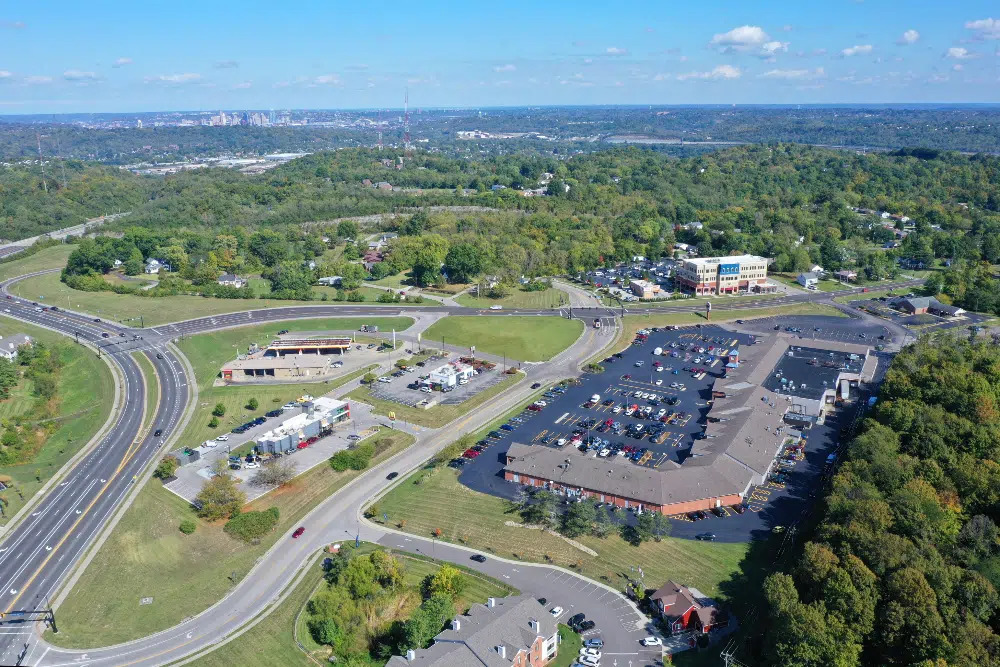 Taylor-Mill-Kentuckyjpg | Route 17 Express Aerial view of a shopping complex with a large parking lot, curved roads, and surrounding trees.