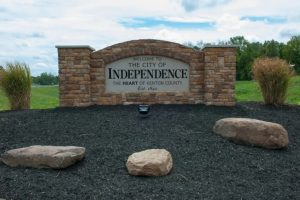 Stone sign reading 'Welcome to the City of Independence' with 'The Heart of Kenton County' on a stone monument and surrounding rocks and shrubs.
