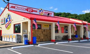 Exterior of Route 17 Express fast-food restaurant with a red roof, hay bales, and patriotic flags in front under a blue sky.